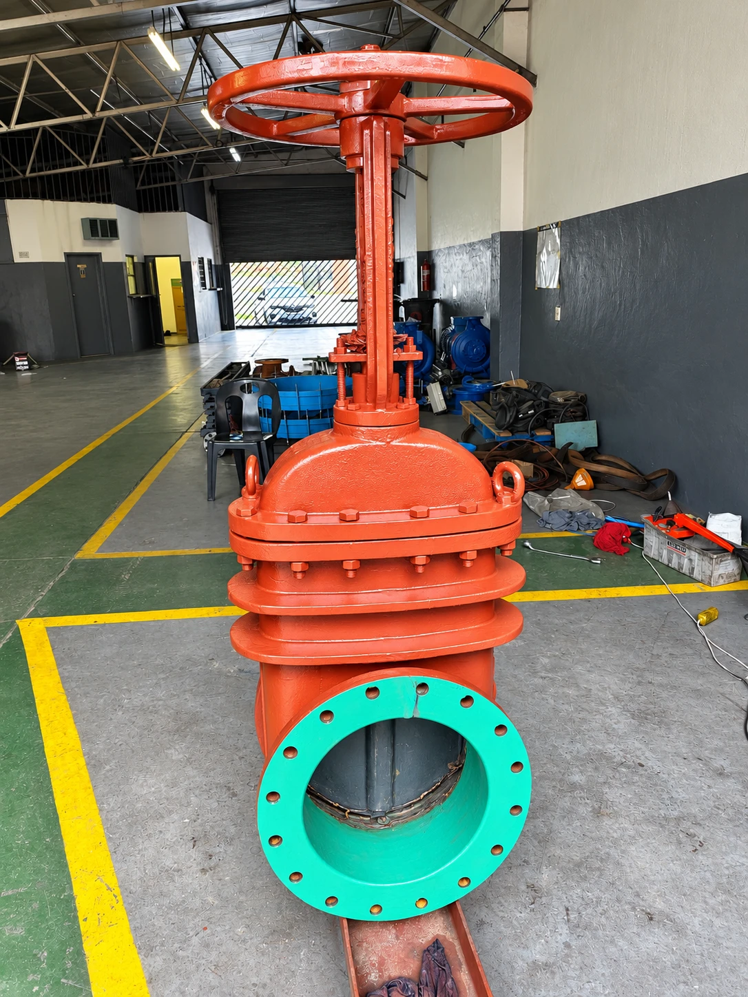 Large red gate valve with green flanges standing on the workshop floor